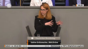Sabine Grützmacher gestikuliert bei ihrer ersten Plenarrede am Rednerpullt des Deutschen Bundestages. Hinter ihr die Bundestagspräsidentin. Es ist ein Screenshot aus dem Parlamentsfernsehen, ein weißes Band läuft am unteren Rand und kündigt die ungefähre Zeit der Abstimmung zu dem diskutierten Antrag an.